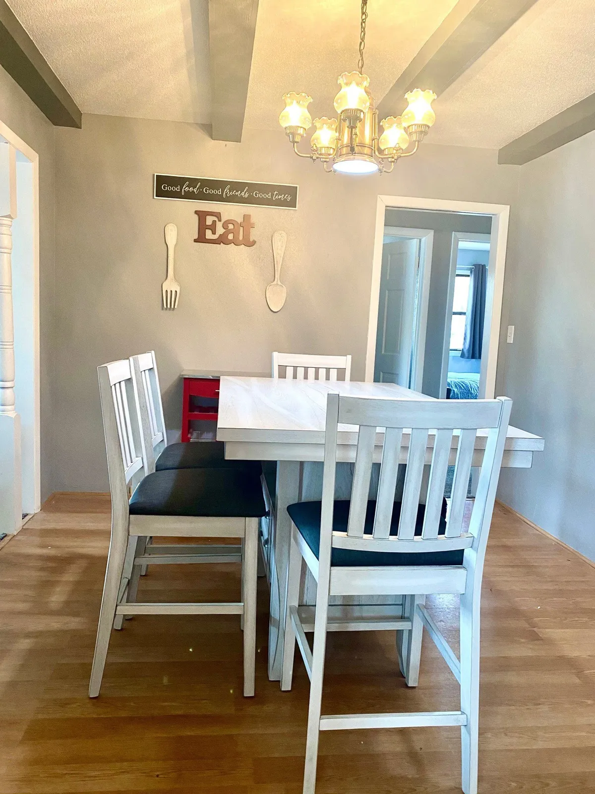 A large dining table sits under a chandelier in a warmly lit room, with a decorative wall sign adding a touch of charm. The space is clearly designed for group meals and festive gatherings, making it perfect for family-style dining.