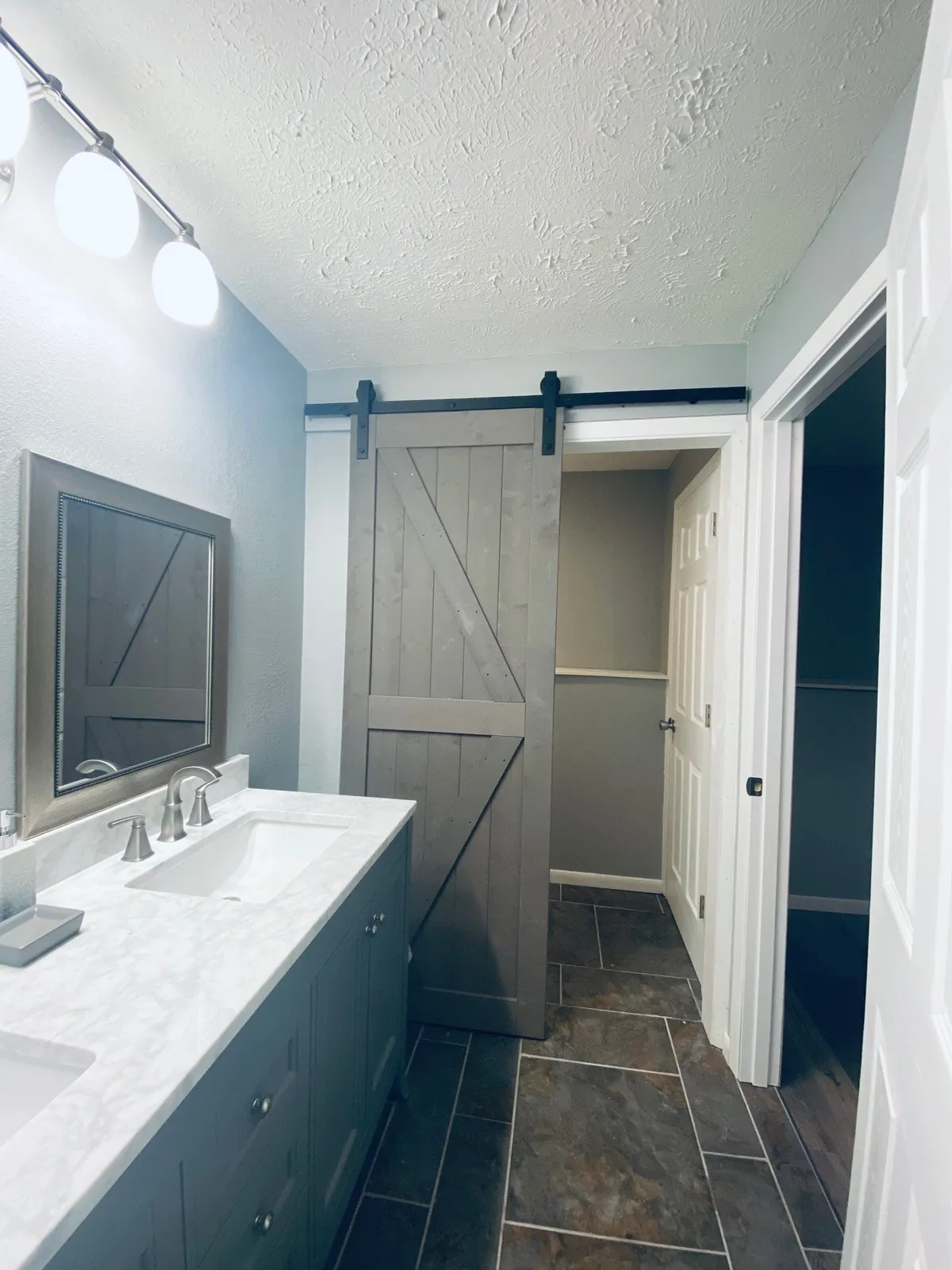 A bright vanity area with a marble countertop, framed mirror, and a sliding barn door, evoking a sense of freshness and serenity. The space is tailored for personal grooming and ease.