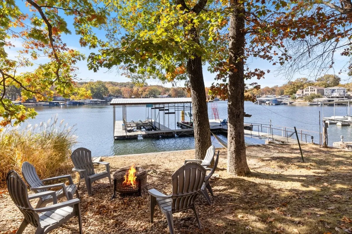 A cozy setup with a fire pit surrounded by adirondack chairs, all facing the lake and a nearby dock. The scene suggests warmth and camaraderie, perfect for gathering at dusk to share stories, roast marshmallows, or watch the sun dip below the horizon.
