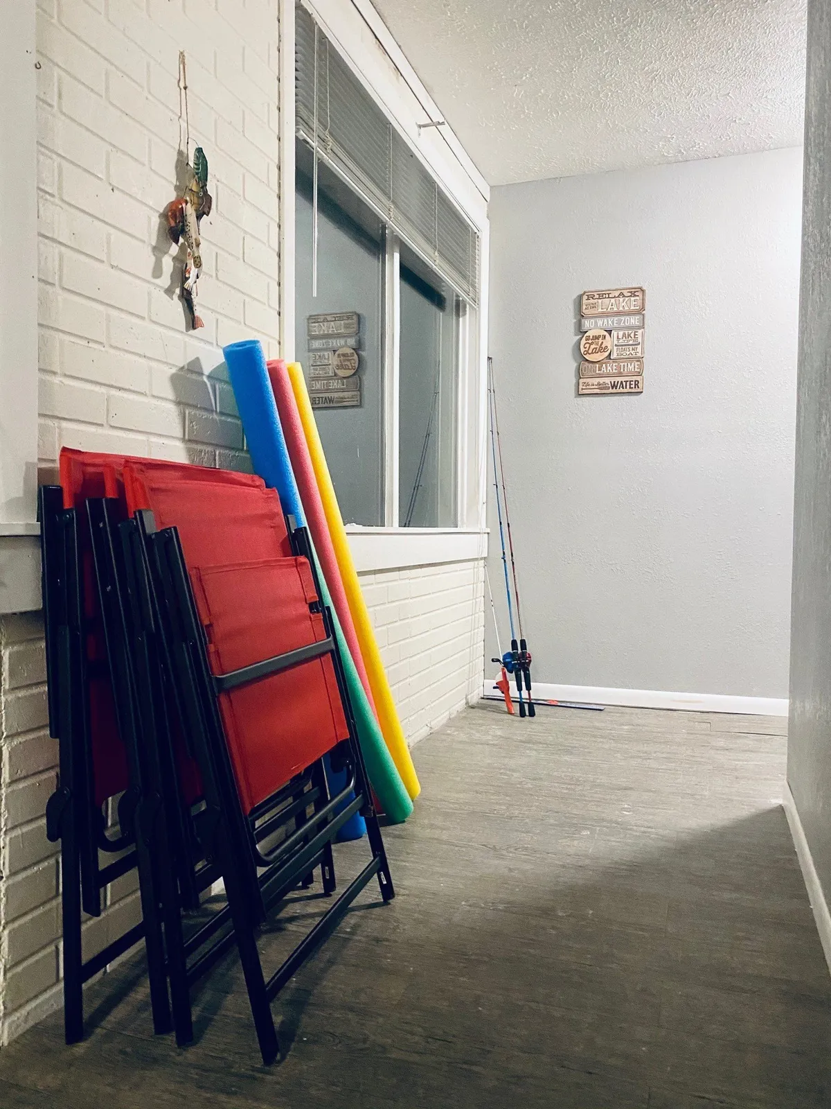 A playful mudroom or entryway with a stack of folding chairs, pool noodles, fishing rods, and decorative wall signs, hinting at organized storage and thoughtful touches that support guest convenience and outdoor activity prep.
