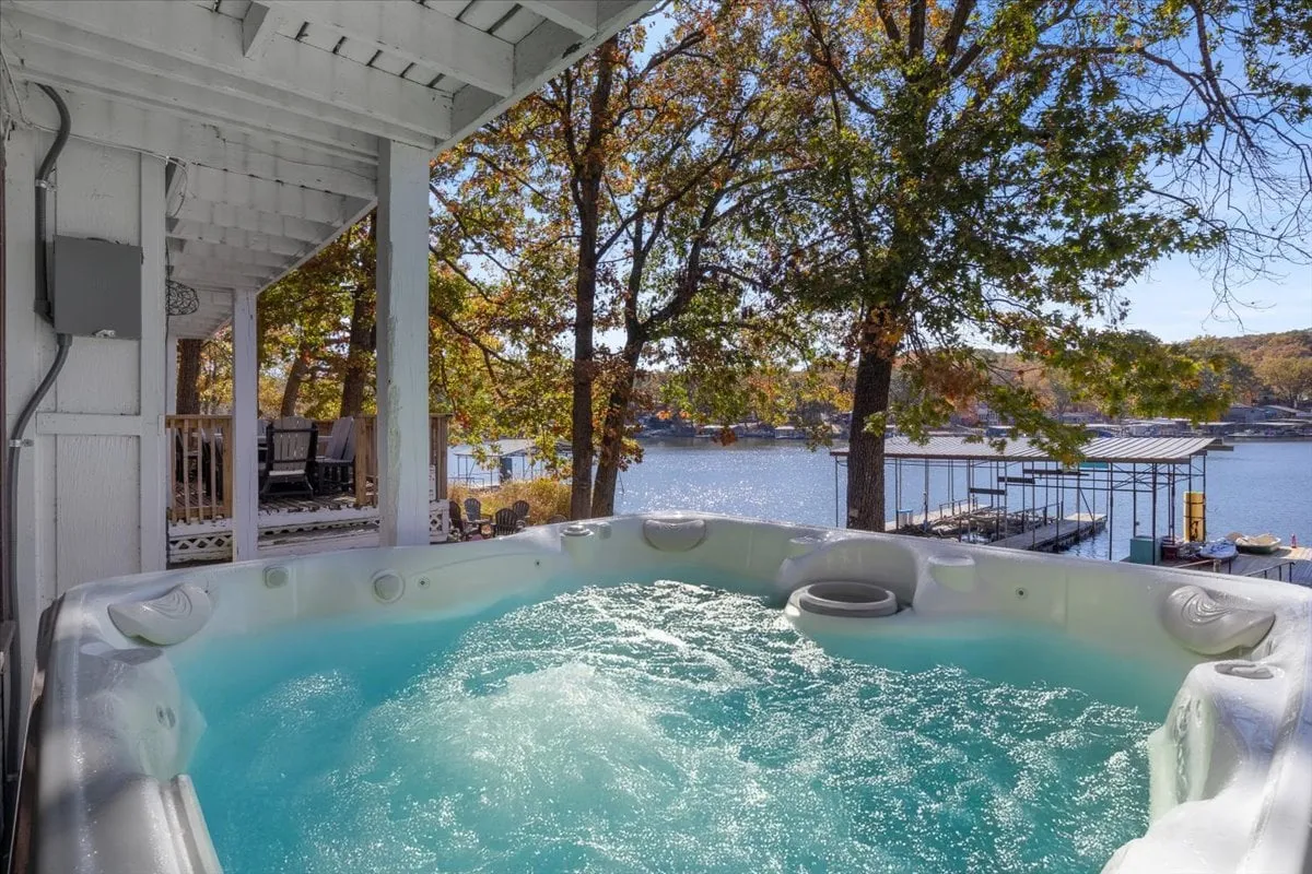 The image showcases the inviting outdoor space of a single-family lakehouse, with a steaming hot tub on a spacious deck overlooking the serene lake, surrounded by lush trees. The scene evokes relaxation and connection, with the promise of beautiful sunsets, tranquil water views, and memorable gatherings in nature.
