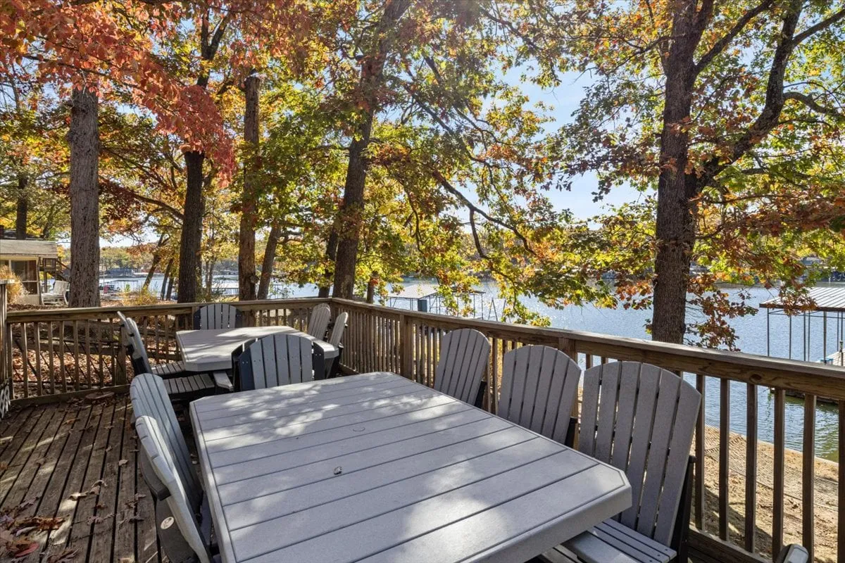 A spacious wooden deck with comfortable seating overlooks a picturesque lake framed by colorful fall foliage. The setting is ideal for dining, relaxing, or reading, with calming water views in the background.