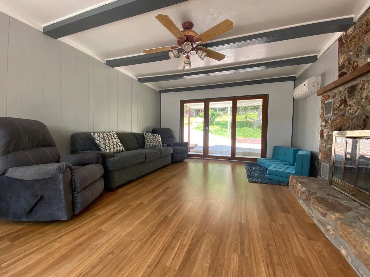 An inviting open-plan living room with plush sofas arranged around a fireplace, large windows letting in natural light, and a ceiling fan above. The room is designed for relaxation and socializing, ideal for game nights or watching TV together.