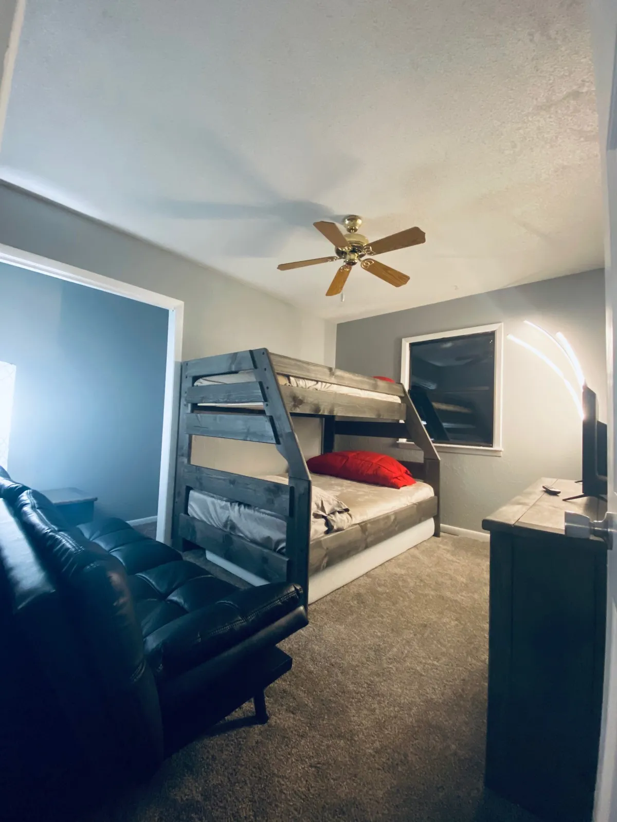 A spacious interior with a bunk bed, leather sofa, floor lamp, and television, creating a flexible space ideal for families or groups. The arrangement invites both sleep and social activities like movie nights or sleepovers.