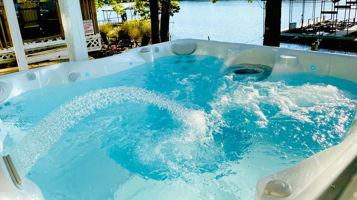 A bubbling hot tub set just above the lake, framed by trees and overlooking the peaceful water, offers a secluded spot for relaxation. The view highlights the natural beauty of the cove, with the hot tub positioned for prime sunset or stargazing experiences.