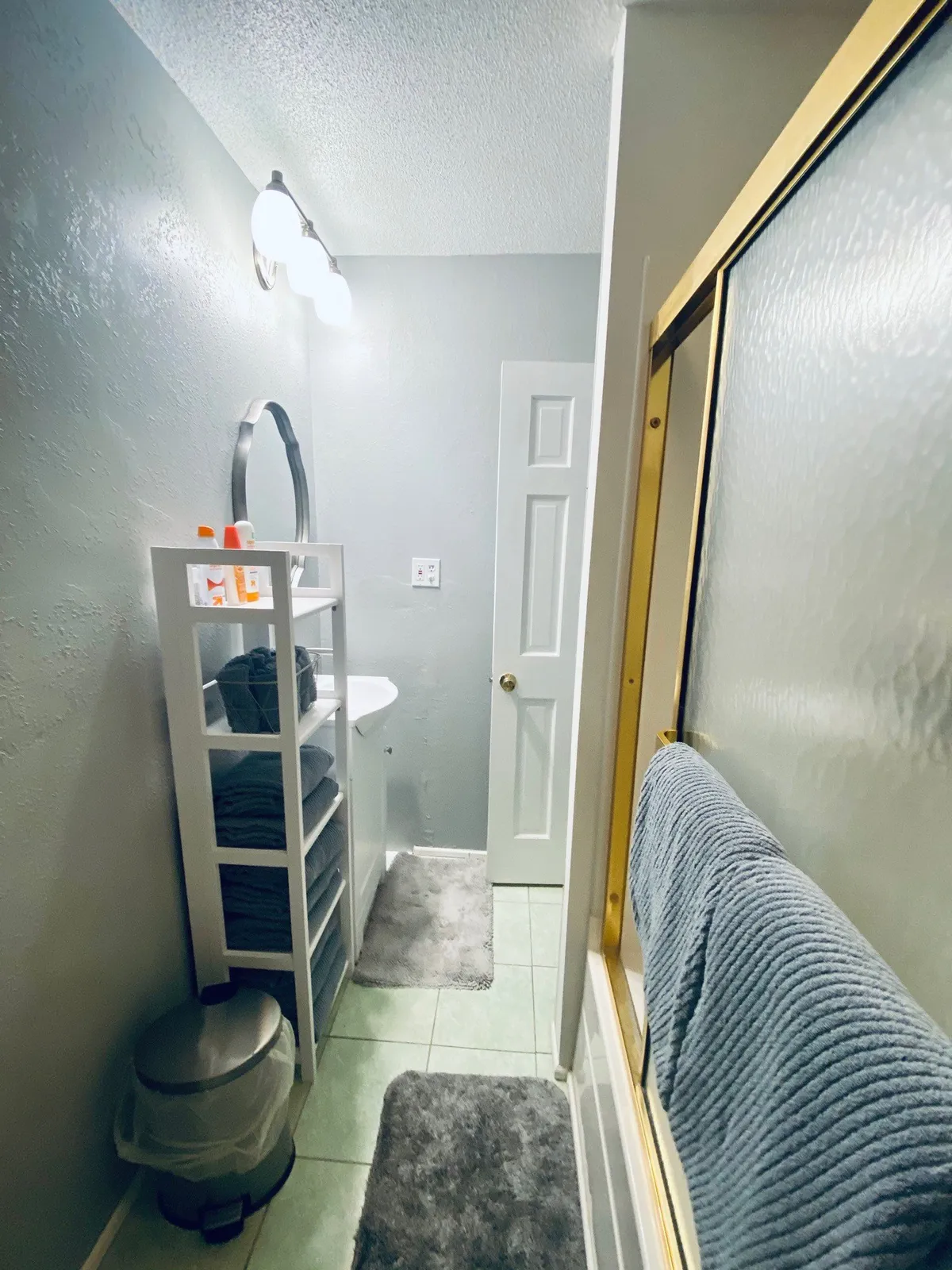 A well-organized bathroom with a large mirror, neatly stacked towels on shelving, and a shower area, all designed with calming colors and a sense of cleanliness.
